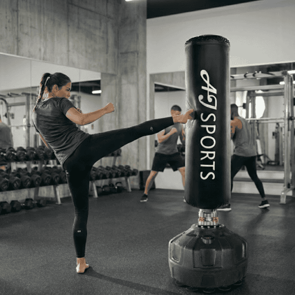 Vrouw die tegen een staande bokszak aan trapt in een gym